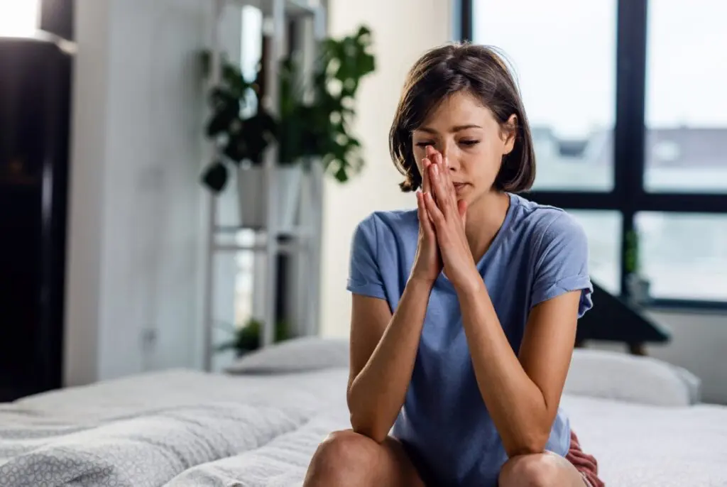 Woman sitting on a bed with hands covering her face, showing signs of stress for trauma counseling.