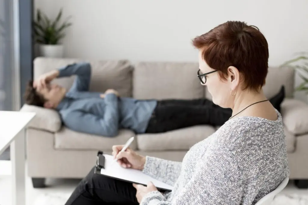 Man lying on a couch while therapist takes notes during an EMDR therapy session.