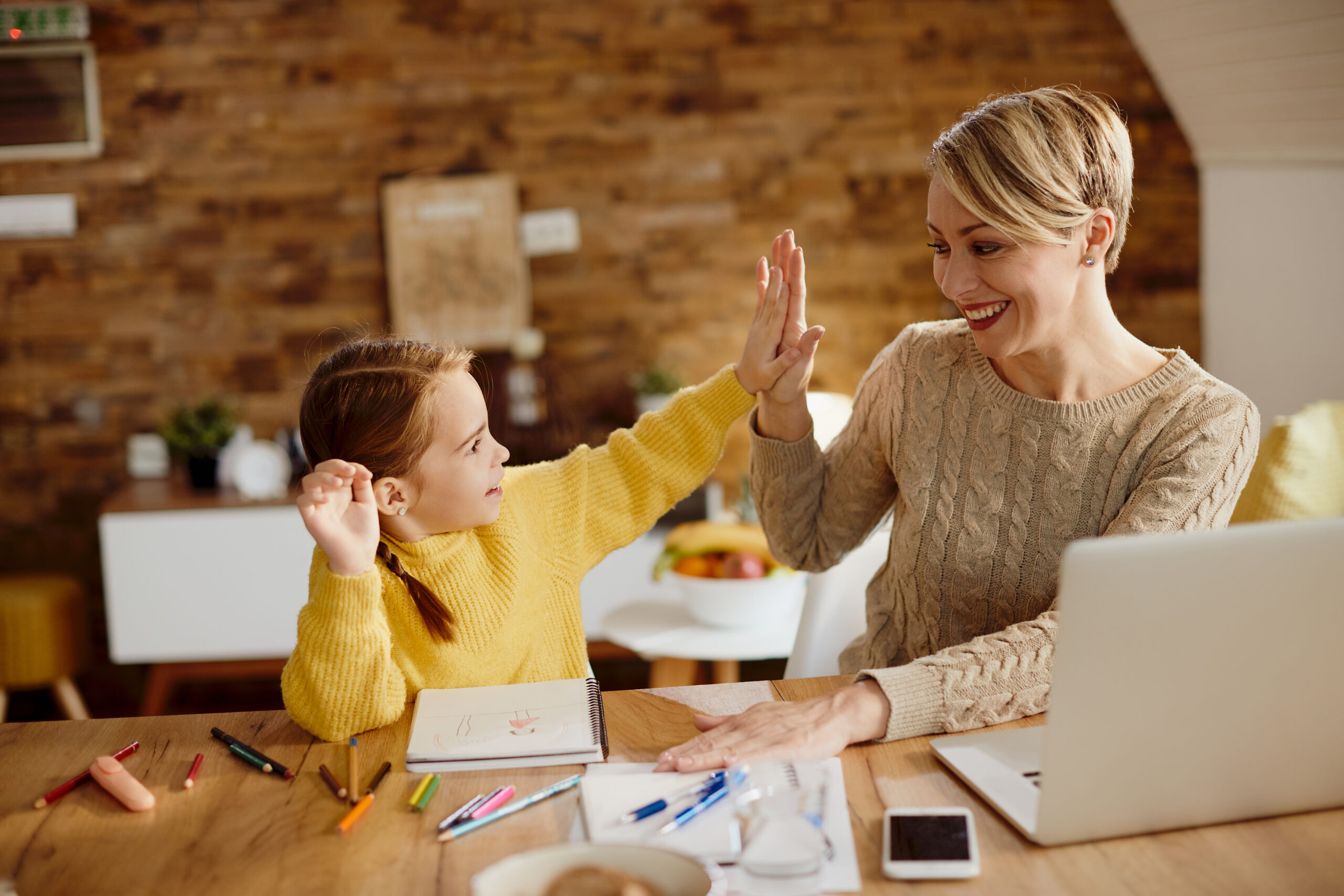 Happy mother and daughter giving high-five during homeschooling.
